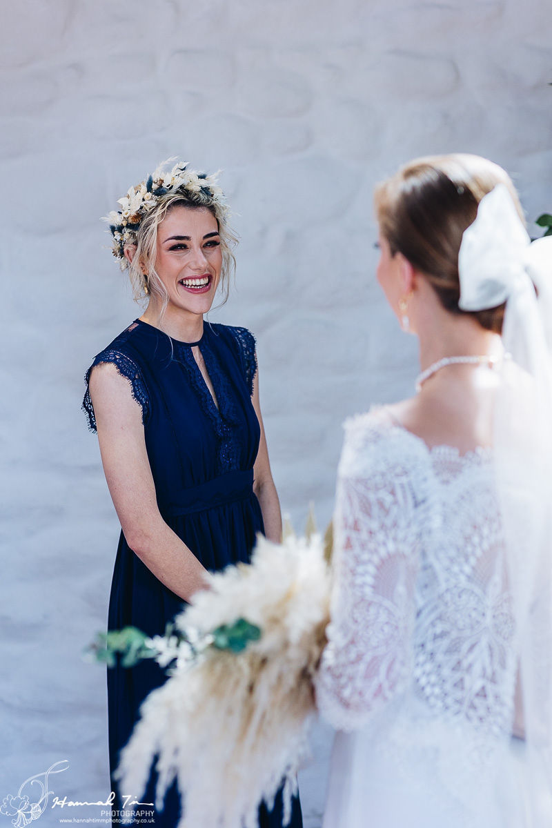 Image of bridesmaid wearing a royal blue sleeveless gown smiling at the bride while wearing a dried flower floral crown