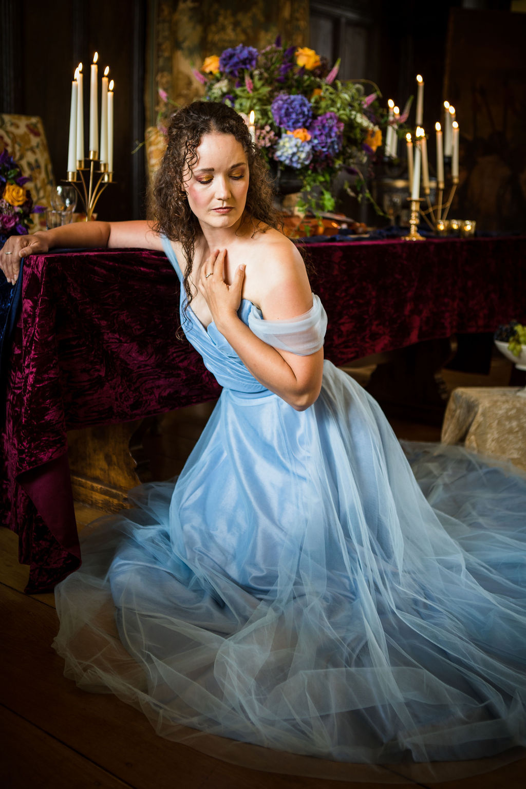 brown haired bride with loose curls wearing a 2 piece blue wedding dress in front of a wedding breakfast table dressed in velvet table cloths in burgandy and navy, golden tableware and vibrant florals